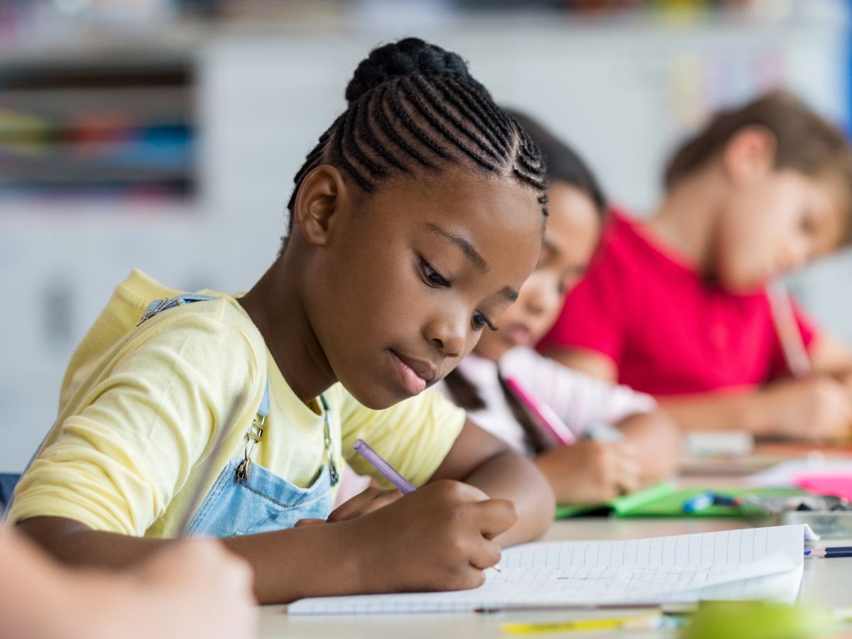 closeup of young girls sitting at desk in school writing while with other kids sitting in background for article 16 Houston Area School Districts