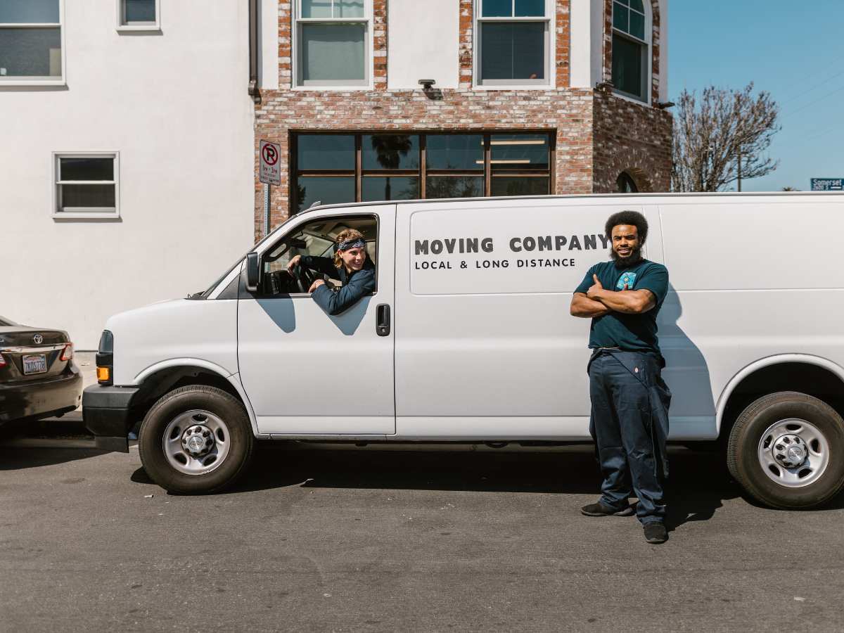 Van that says moving company for local and long distance moving with one person in drivers seat and one standing in front of the van with arms crossed for article 15 Critical Tips for Hiring a Moving Company for newcomers moving to Houston.