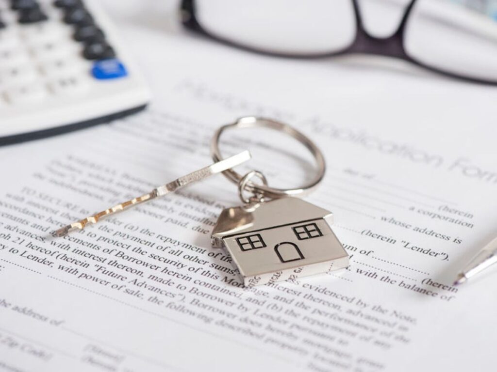 Close up of an application with part of a calculator and glasses at the top and a key on a keyring that is in the shape of a house for article Obtaining a Mortgage in Houston for newcomers moving to Houston.