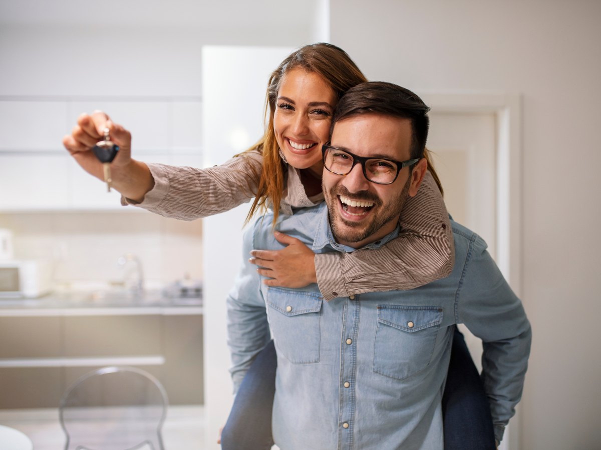 Pictured woman on the back of her husband hugging him and holding out new house key for article Services And Utilities in Houston