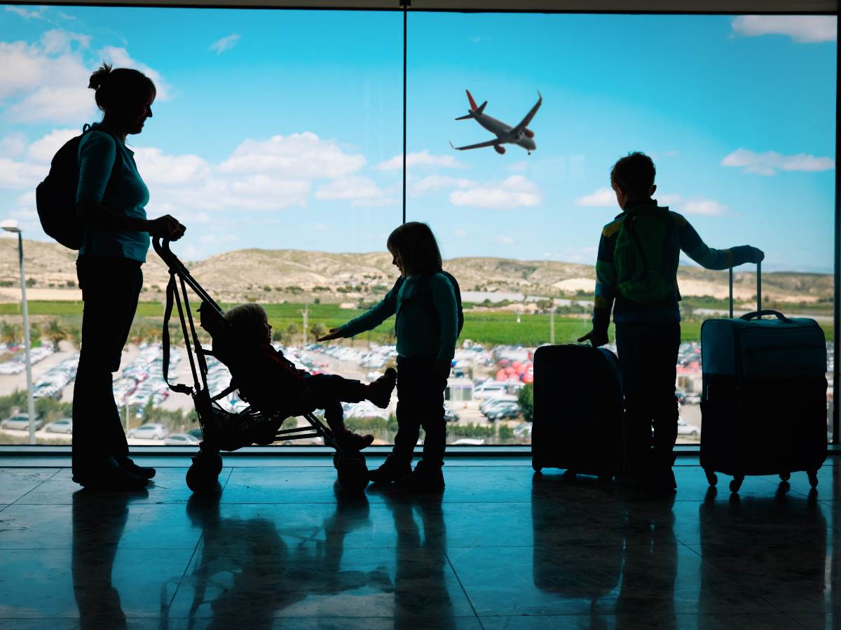 Silhouette of Mom and 3 kids - 1 child is in stroller, 1 is playing with child in stroller, and 3rd child is holding roller suitcase handles for article International Relocation to Houston for newcomers moving to Houston.