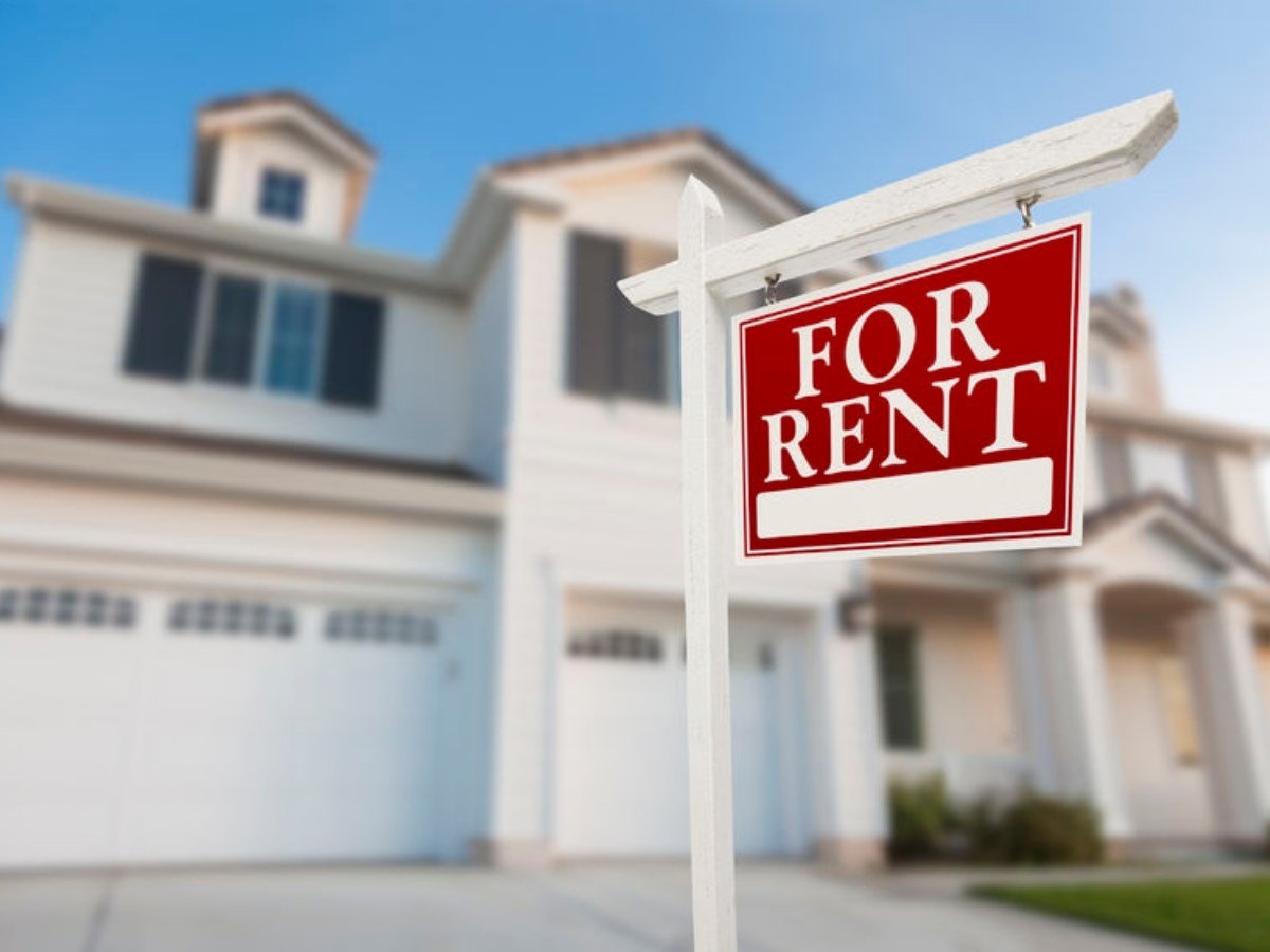 Blurred house in background with red and white FOR RENT sign in front for article Renting a home in Houston.