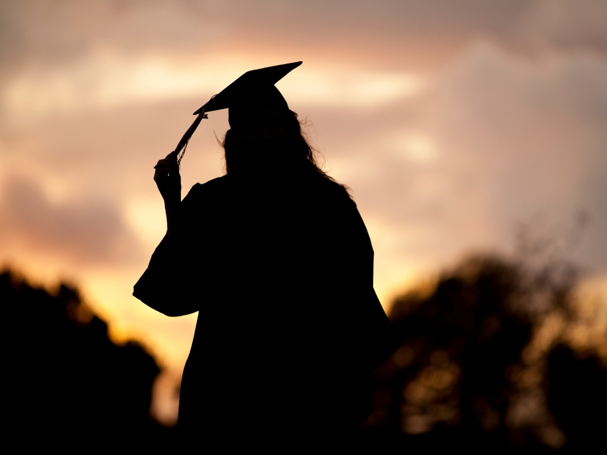Silhouette of a high school graduate in cap and gown with sunset in background for article Splendora ISD