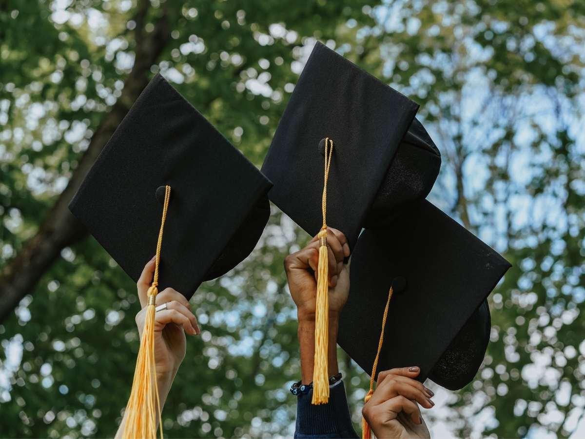 3 hands holding up graduation caps with trees in background for article Sheldon Independent School District