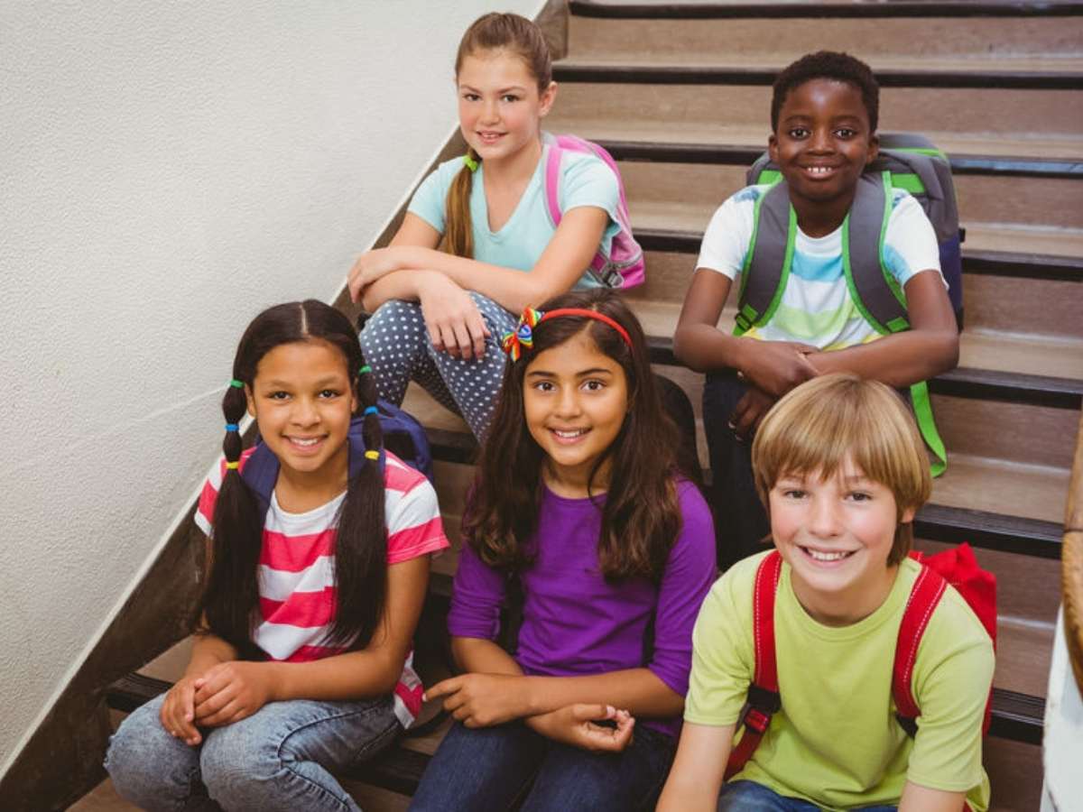 Group of 5 young diverse students with backpacks on sitting on stairs posing for photo for article New Caney Independent School District