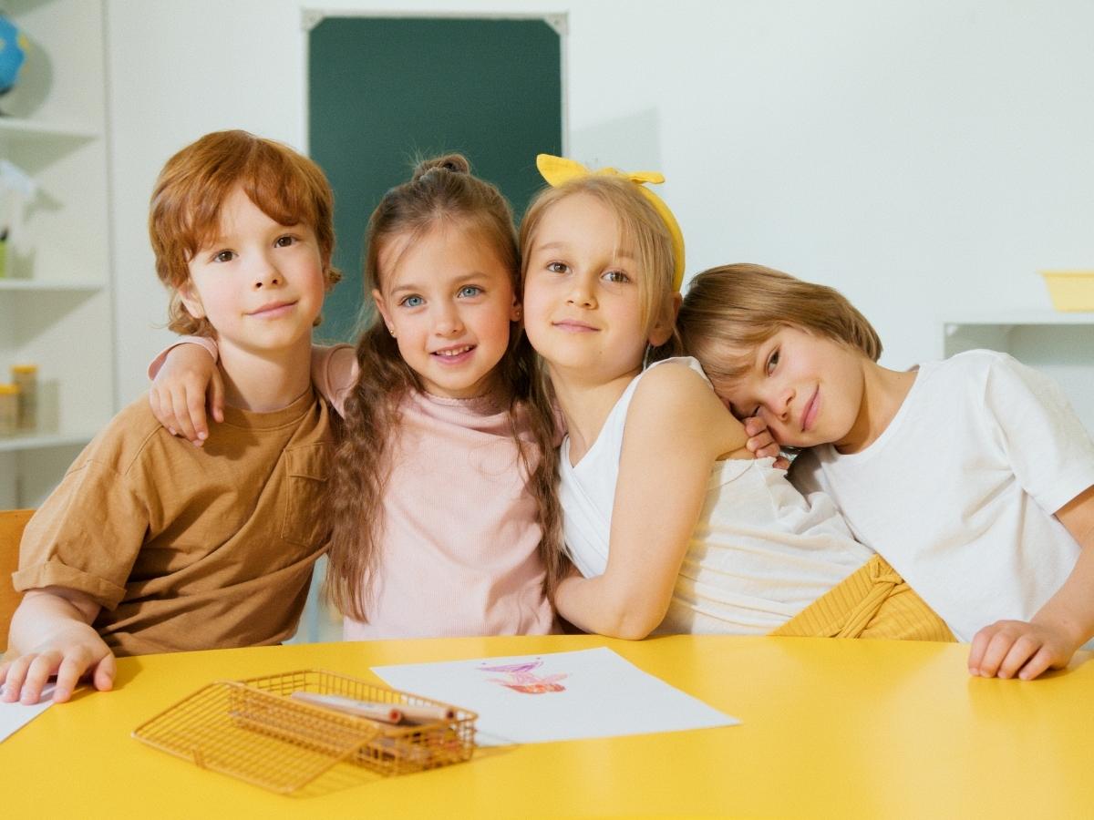 4 kids sitting at yellow table in classroom posing for camera for article Goose Creek CISD