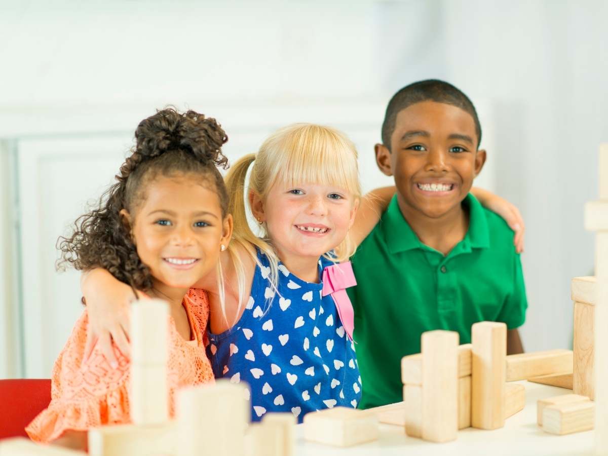 3 Kids posing for picture in classroom with wooden building blocks for article Crosby ISD