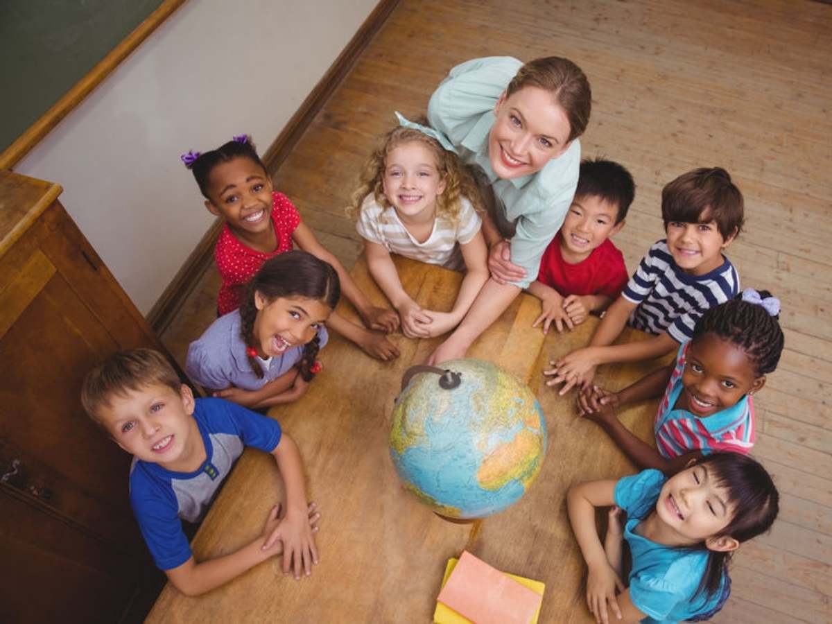 Diverse group of young kids sitting around a table with a world globe in it looking up at the camera for article Houston Area Education