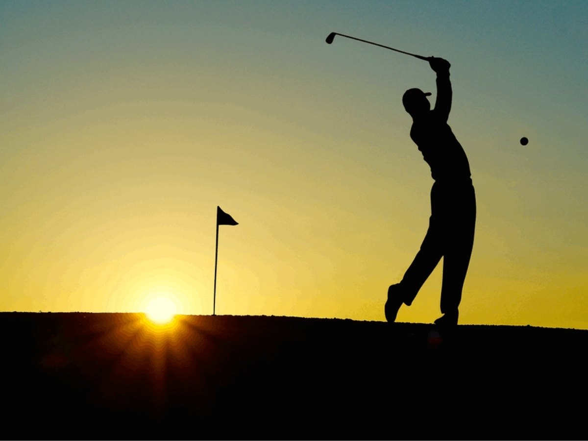 Silhouette of golfer swinging his club at sunset with the pin flag and sun setting on the horizon for article Northeast Houston Golf Courses