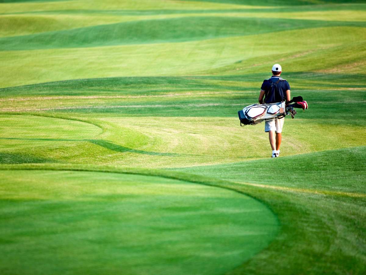 Bright green golf course with golfer carrying bag and walking away from camera in the distance for article 15 Trending Houston Area Golf Courses for newcomers moving to Houston.