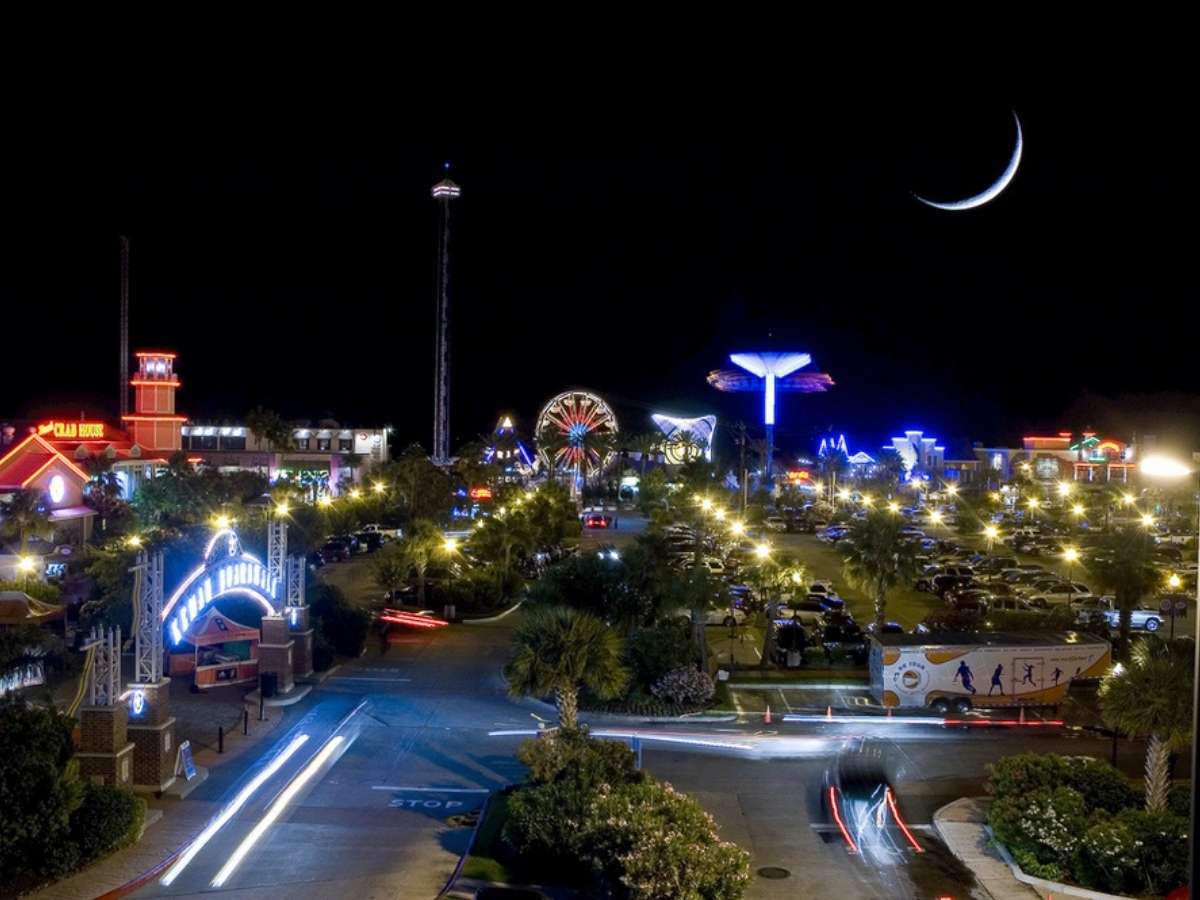 Kemah boardwalk lit up at night with rides glowing and a sliver of a moon for article Kemah, Seabrook and Webster for newcomers moving to Houston.