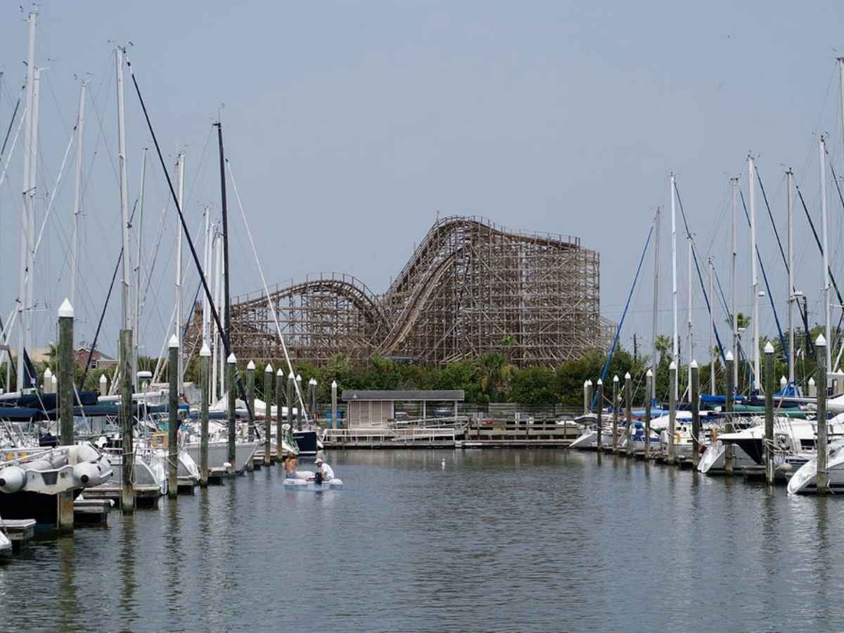 Sailboats docked on either side and rollercoaster in distance at Kemah Boardwalk for article Clear Lake for newcomers moving to Houston area.