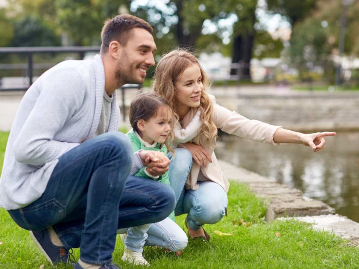 Couple kneeling down with their daughter looking over concrete edge of water pointing out toward water for article Spring for newcomers moving to Houston area.