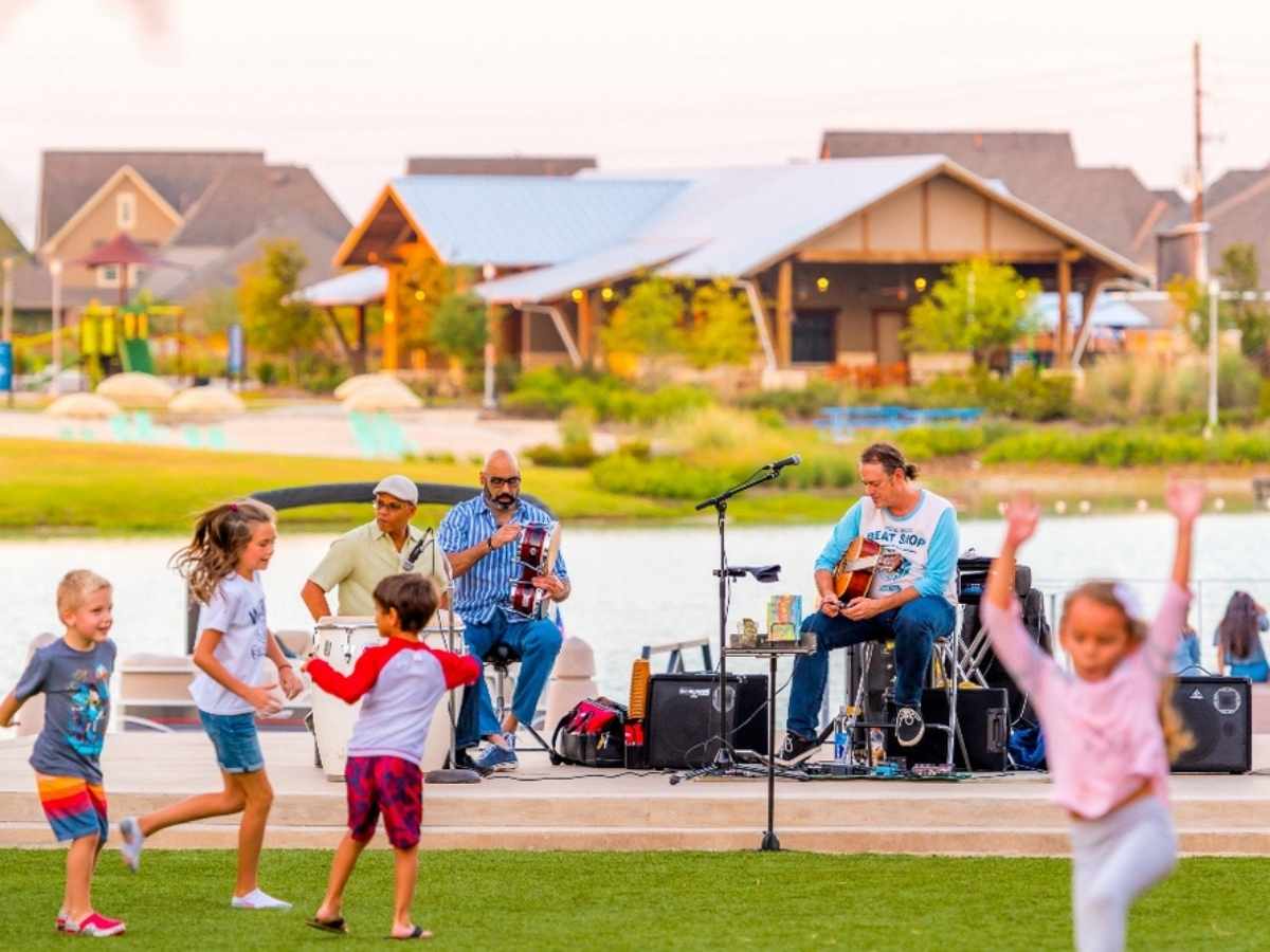 Kids playing in grass, while band plays on concreter overlooking Boardwalk Towne Lake for article Cypress Fairbanks for newcomers moving to Houston.