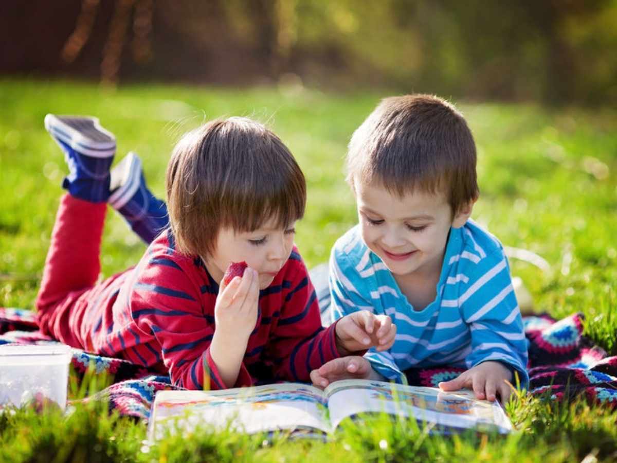 2 kids laying on the ground reading a book for article Aldine for newcomers moving to Houston area.