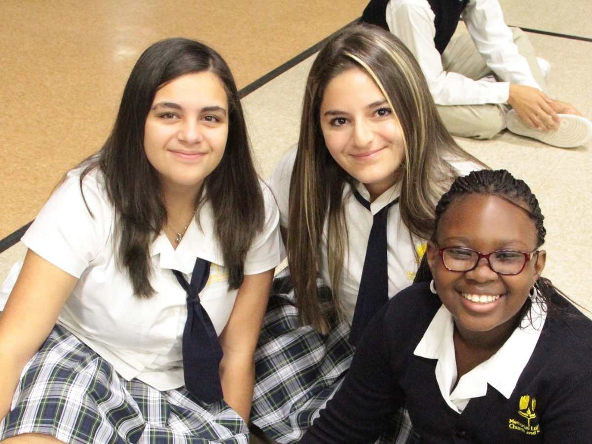 3 girls sitting on basketball gym floor in their school uniforms smiling for camera for article Memorial Lutheran School