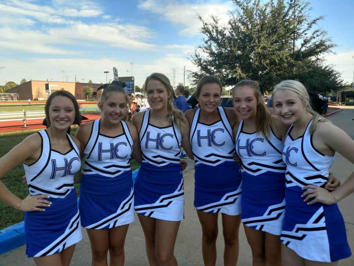 6 Cheerleaders in blue and white uniforms in a line with their arms around each other posing for picture for article Houston Christian High School