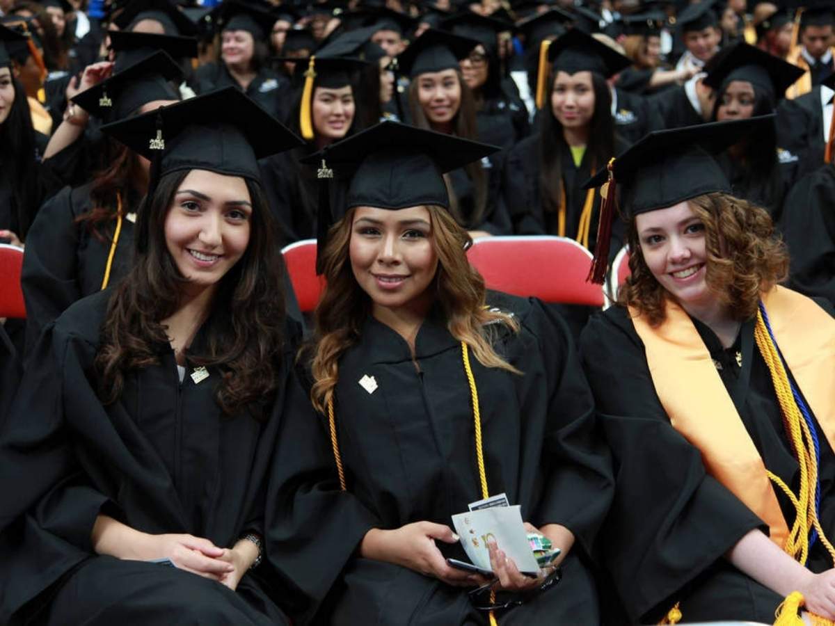 Graduates in cap and gown sitting at graduation ceremony - 3 in front posing for photo for article Houston Community College for newcomers moving to Houston.