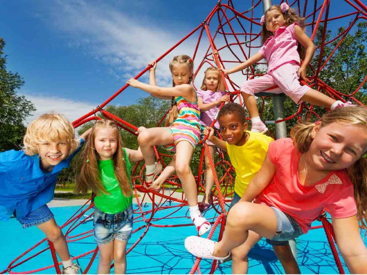 7 kids playing on a red cargo net on playground with blue background for article Briar Forest for newcomers moving to the Houston area.
