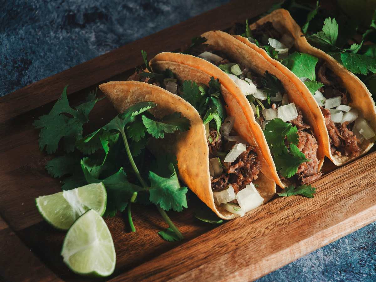 Tacos on a wood plank with garnish and limes on the board for article Best Food Tour in Houston for newcomers moving to Houston.