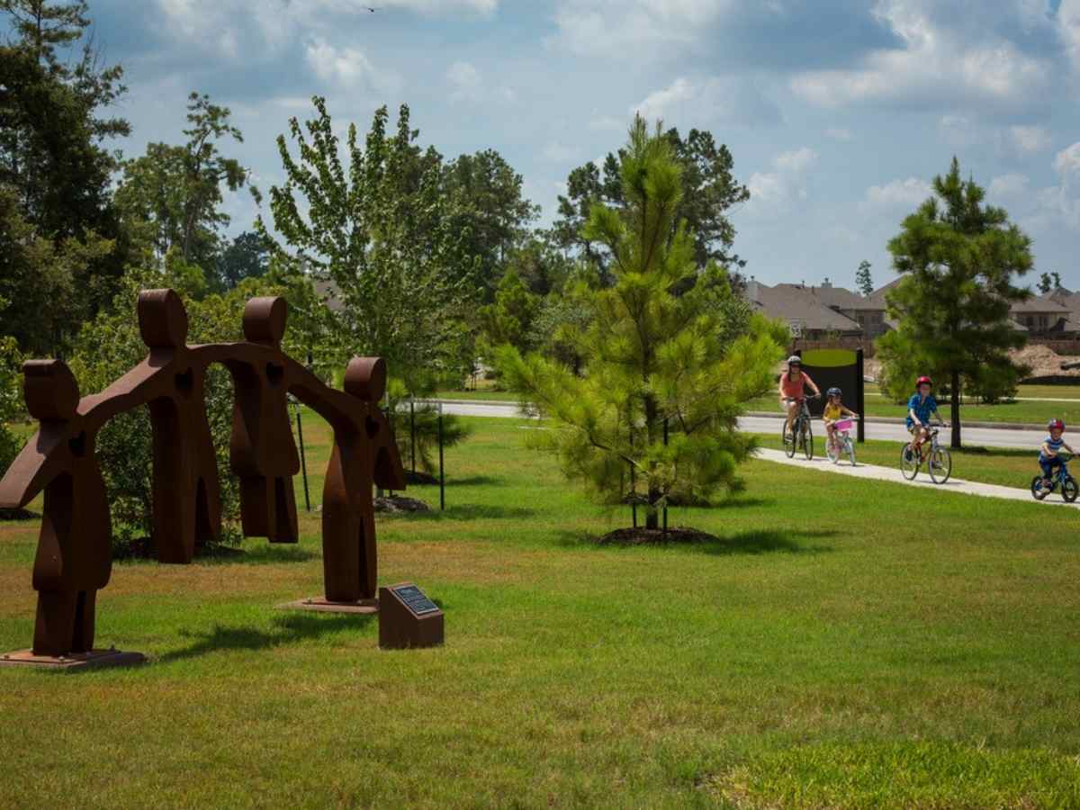 Outdoor park area with people shaped statues that are connected and family riding bikes on path for article Harmony Ranked as Nation’s Fastest-Growing Top-Selling Community for newcomers moving to Houston area.