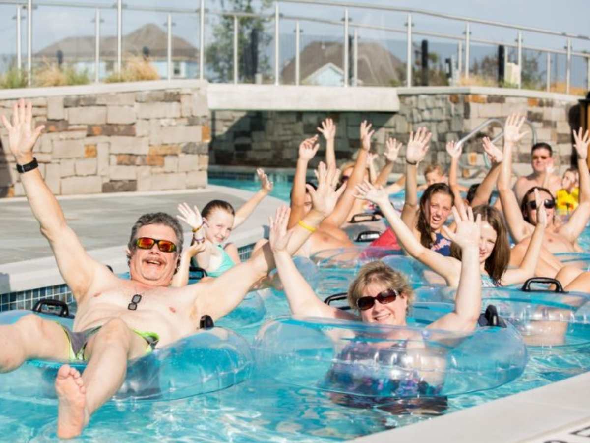 Group of people with inner tubes in pool river holding hands up for article Lazy River in Jordan Ranch