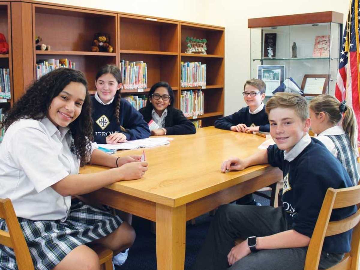 6 Students sitting at a table in a library for article St Jerome Catholic School for newcomers moving to Houston.