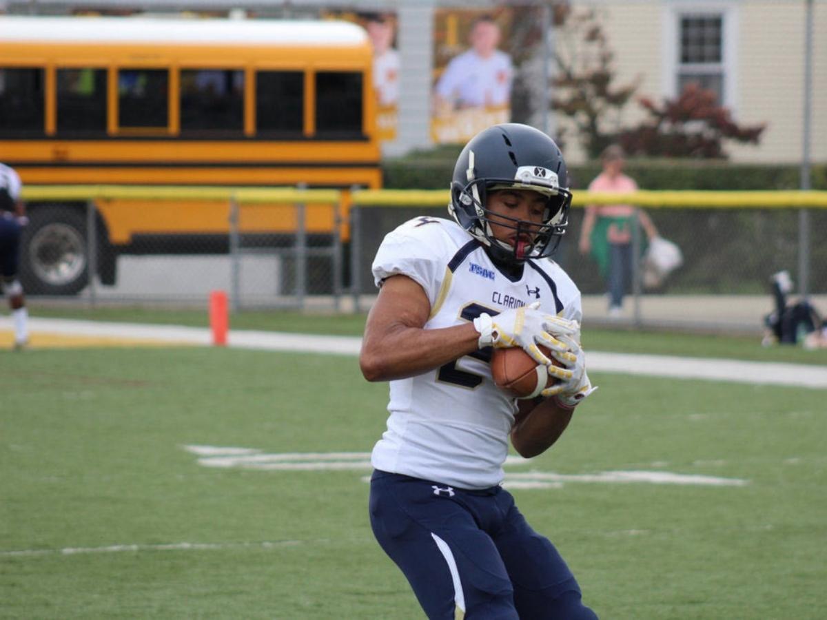 Football player catching football on field with school bus in background behind field for article Education in West Houston