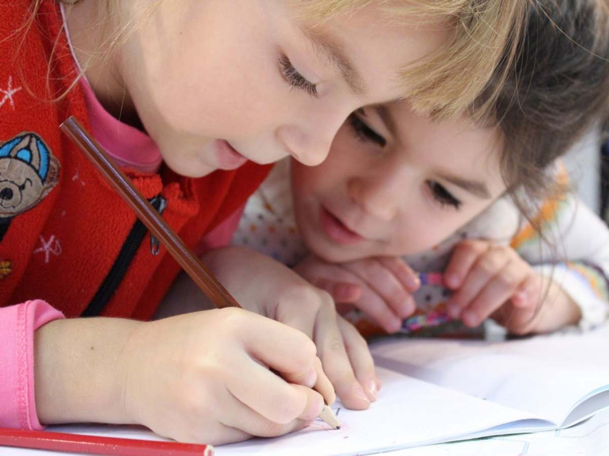 2 young kids leaning in over desk watching one of them color with a colored pencil for article Education in Montgomery County