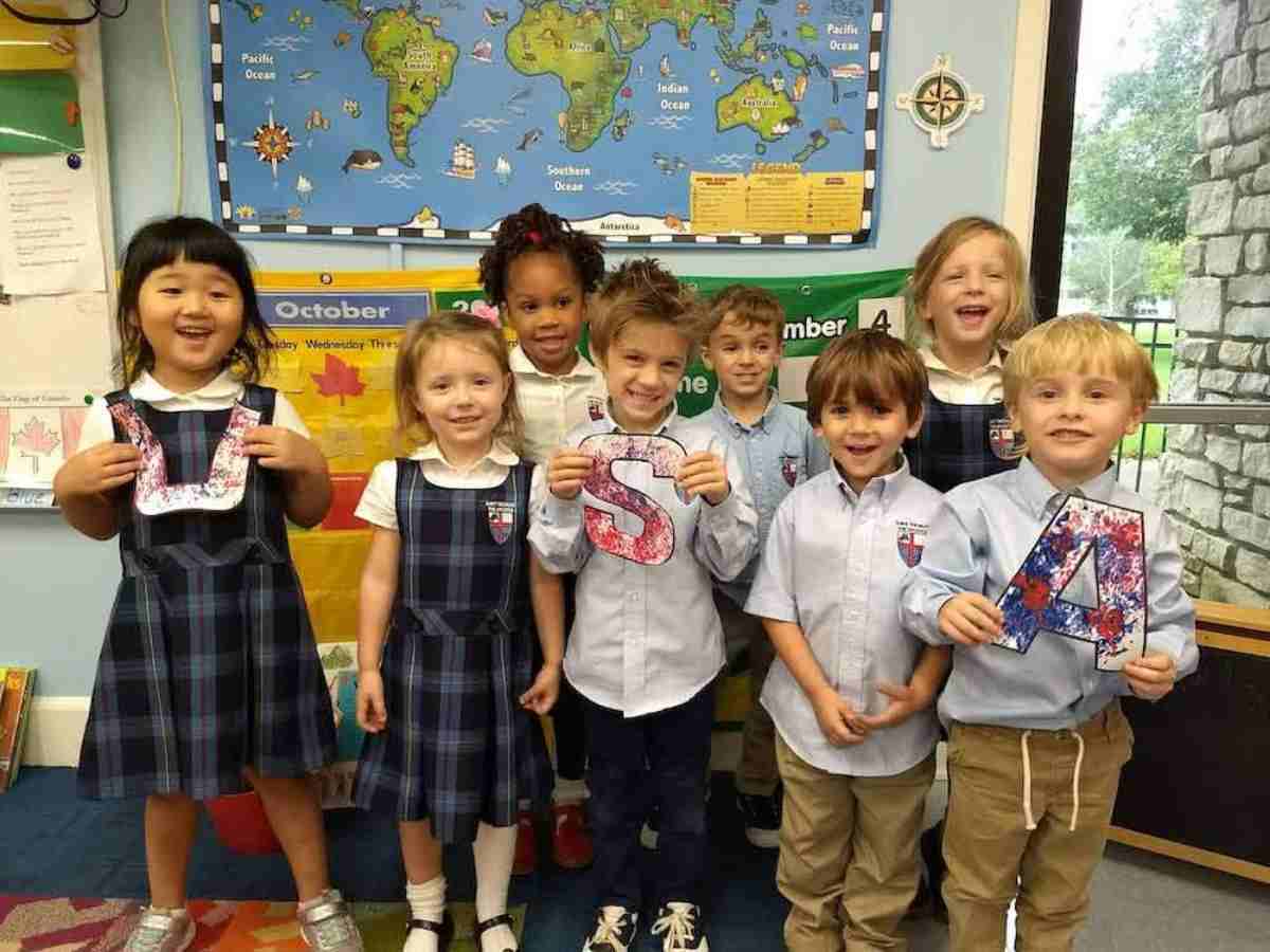 Group of young students in school uniforms posing for photo and holding up cutouts of the letters USA that are creatively painted in red, white, and blue for article St Thomas the Apostle Episcopal School