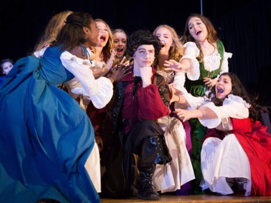 School musical with gilrs dressed in long olden day dresses and 1 boy kneeling in center for article Calvary Episcopal Preparatory