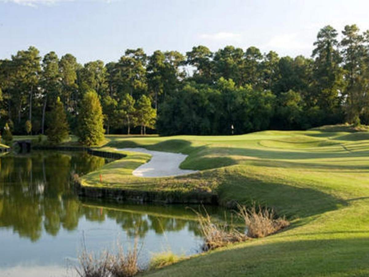 A golf course with greens, sand trap and water obstacle and trees in background for article The Clubs of Kingwood