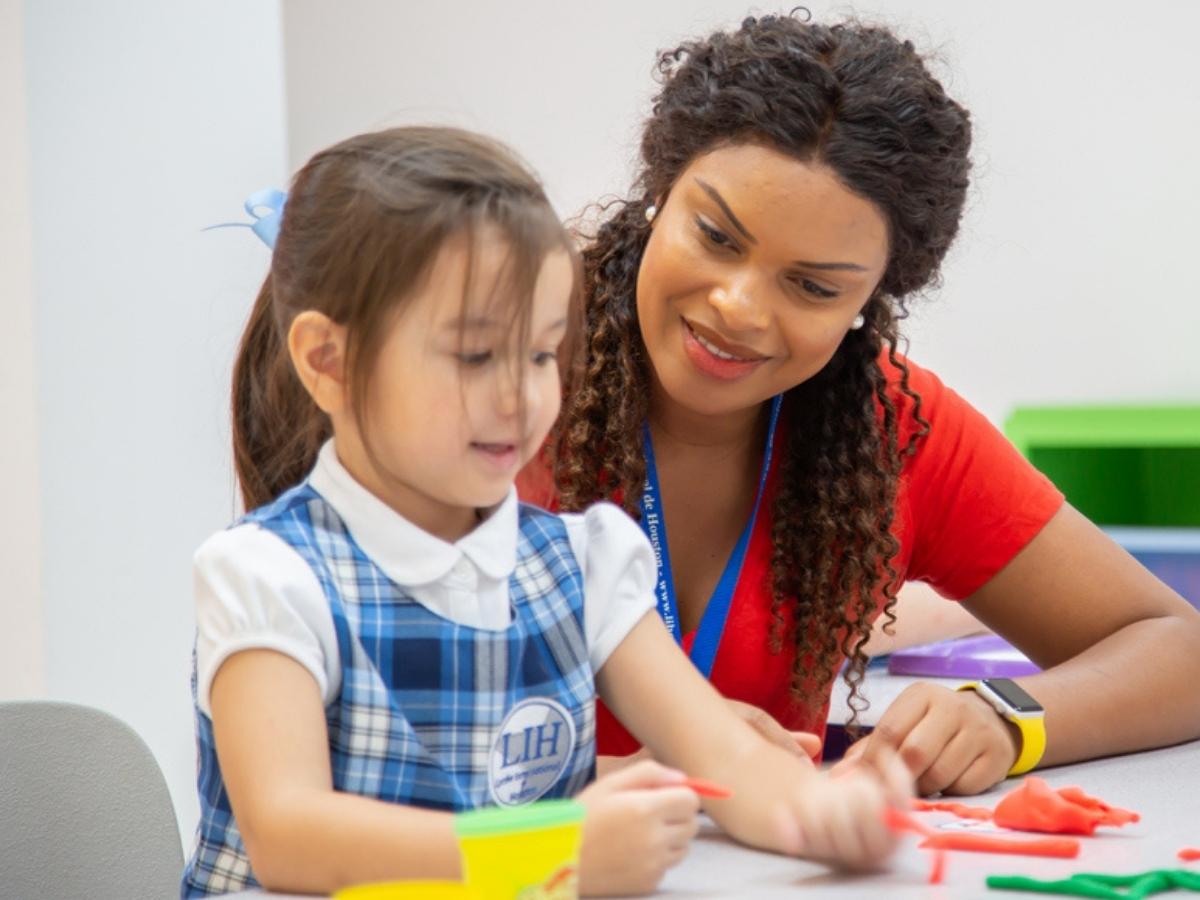 Teacher sitting at table helping a student who is in a LIH school uniform for article The Lycée International de Houston: Bilingual School