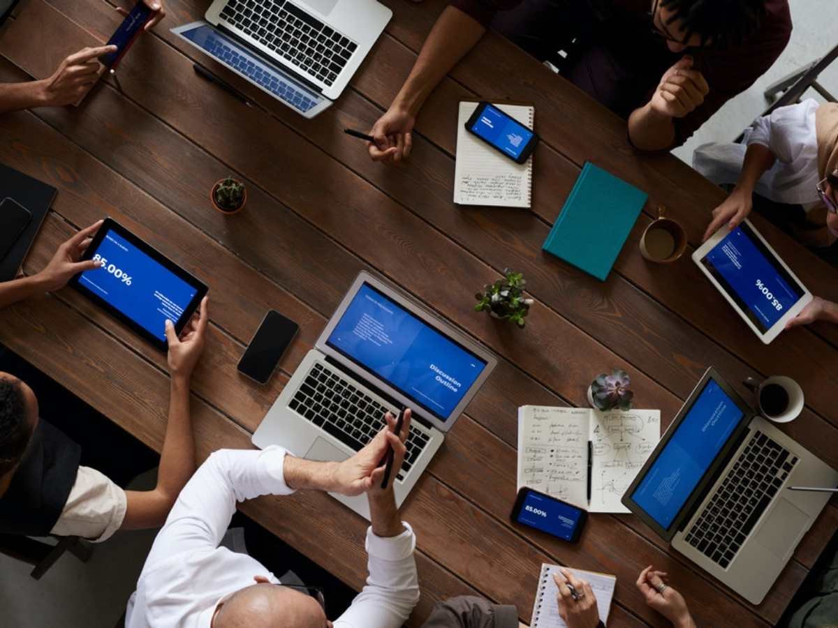 Aerial view of conference table showing people holding tablets and working on laptops for article HCC Workforce Program