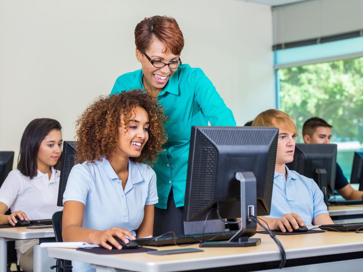 High school students working on computers with teacher over should of one student helping for article Top 20 Private High Schools in Houston for newcomers moving to Houston.