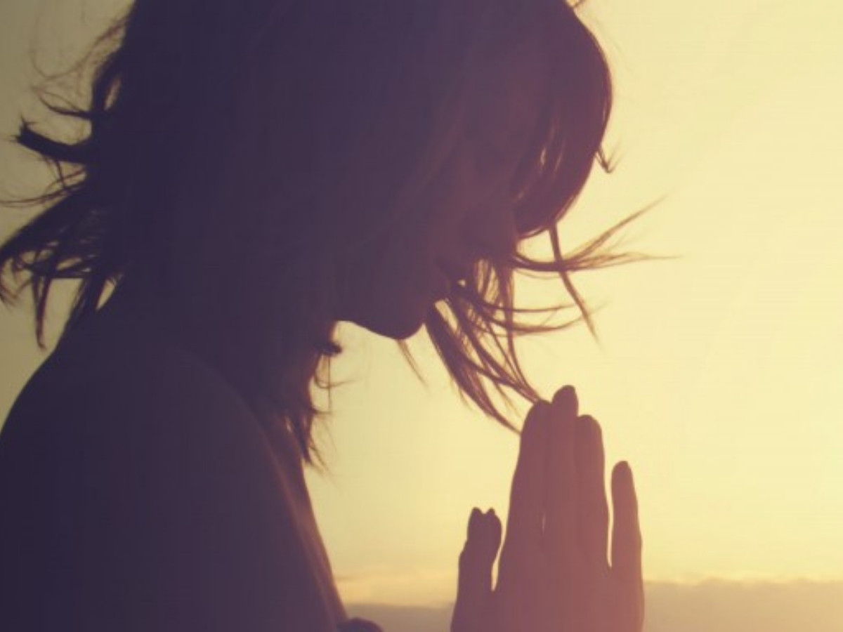Silhouette of profile of woman with hands together for prayer with hazy yellow background for article Places of Worship in Fort Bend