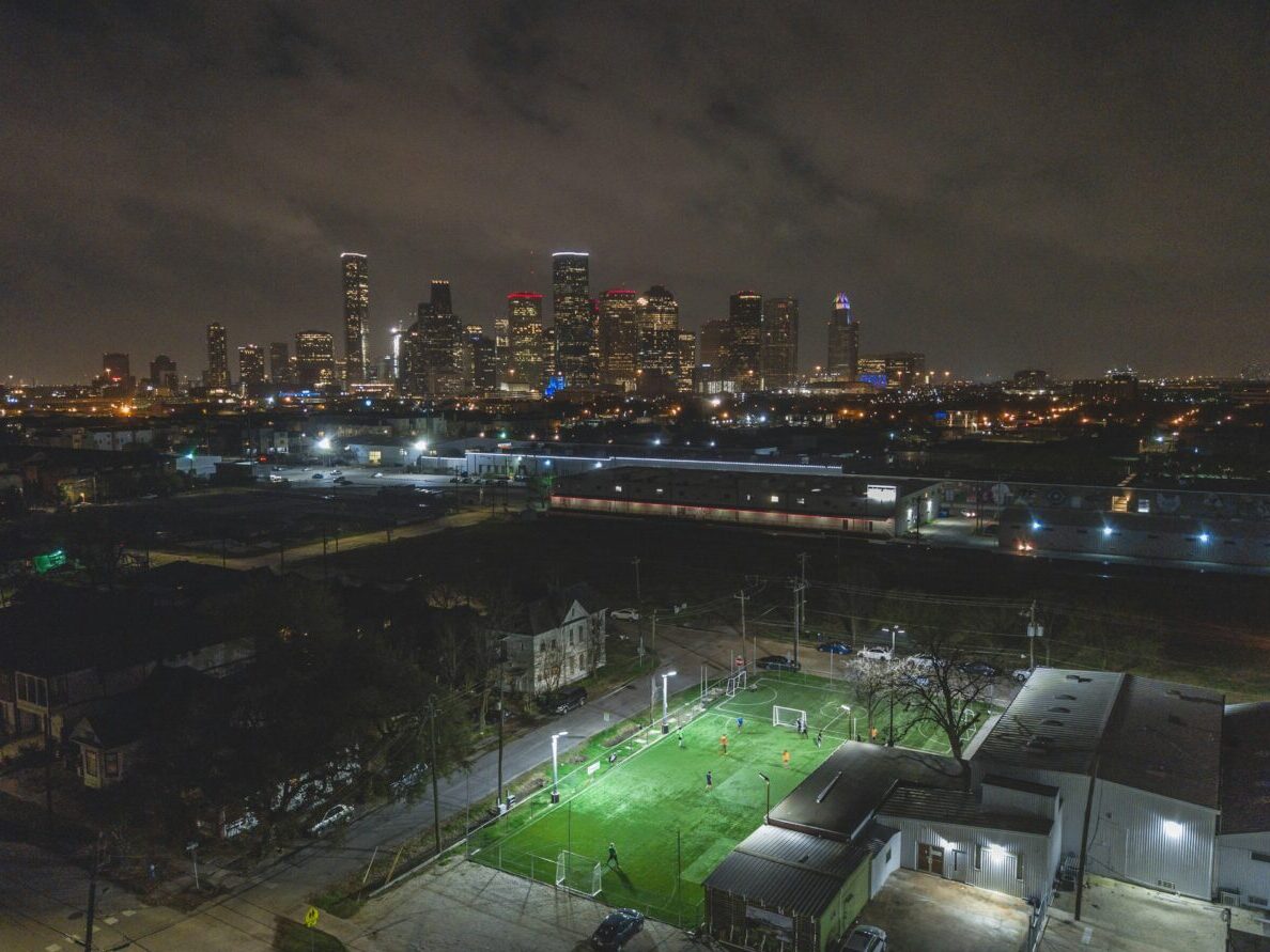 bird's eye view of a football stadium lit up at nighttime while viewing the Houston skyline in the distance for article Houston reaches the Top 10 of U.S.News's The Hottest US Housing Markets list!