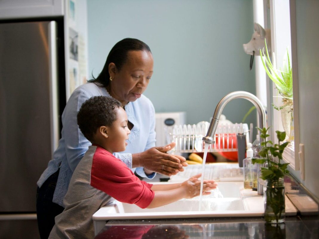 mother is showing the process of teaching her young son how to properly wash his hands at their kitchen sink