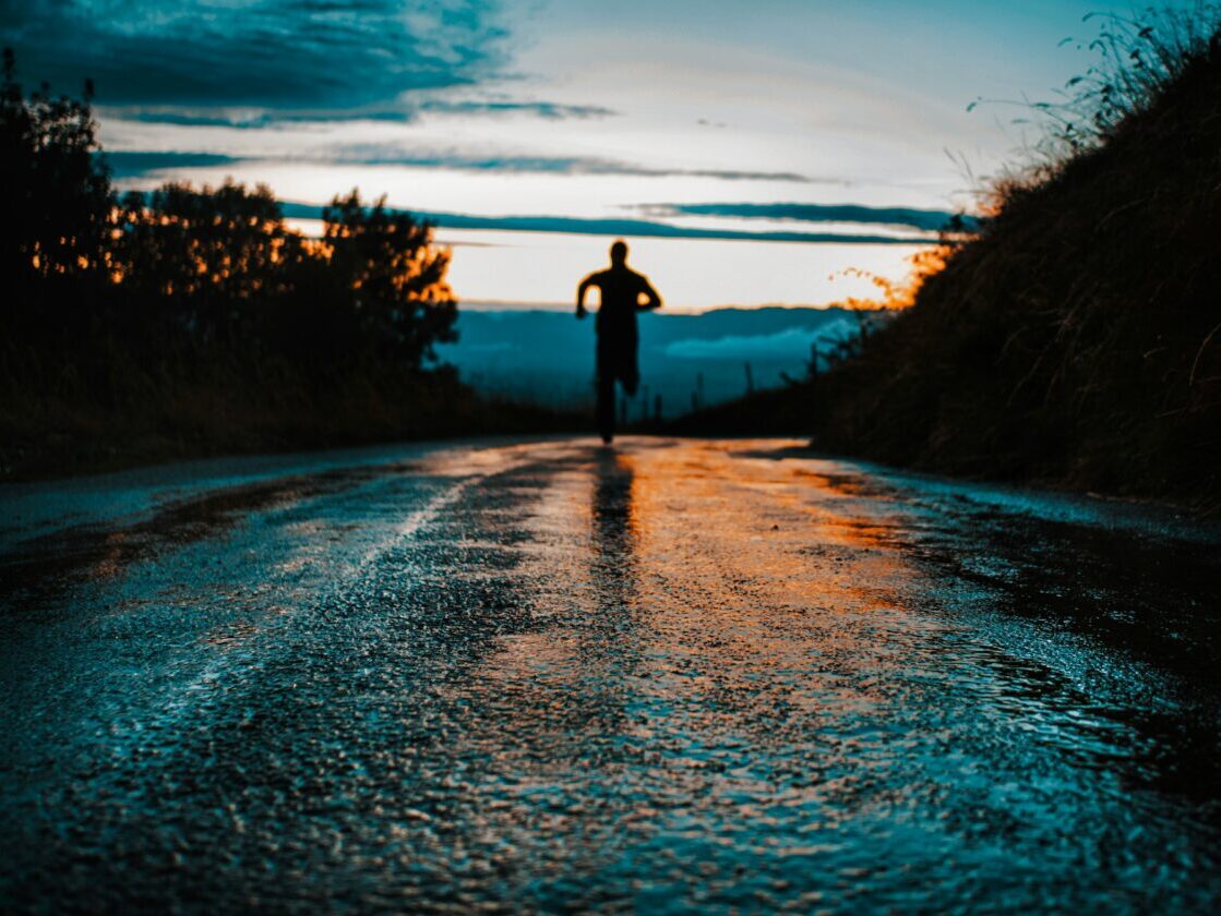 a person running towards sunset on a rainy road