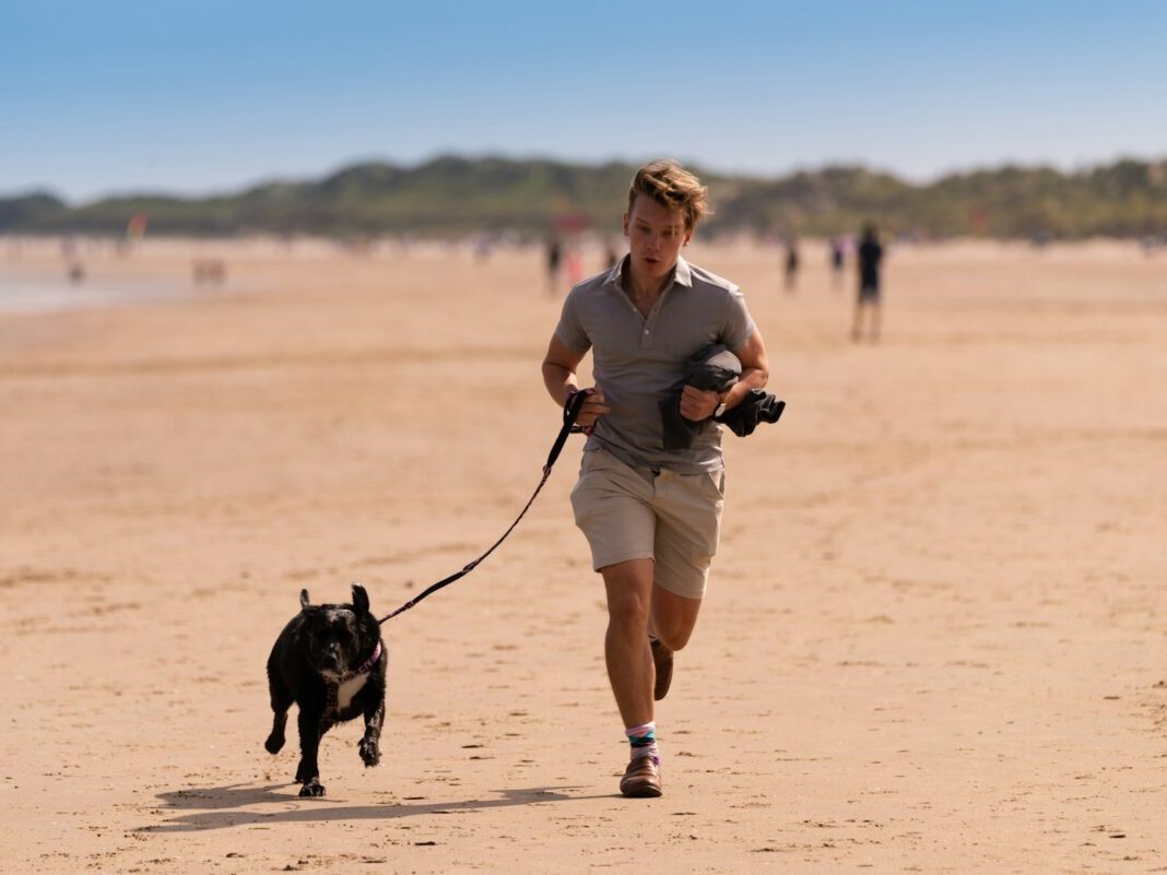 Person running the beach holding a leash to small black dog