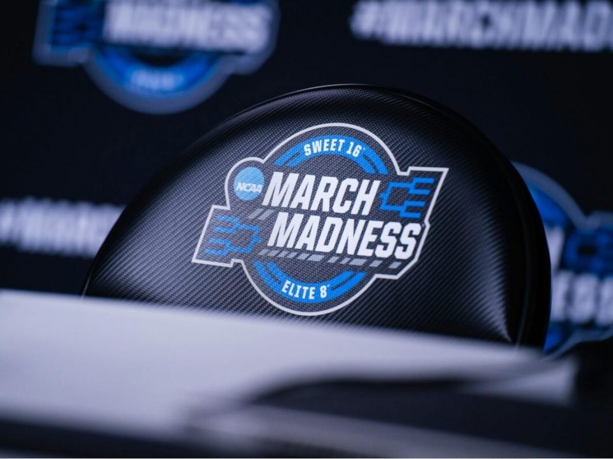 an NCAA black folding chair with the March Madness logo in blue sitting behind a desk for article Men's & Women's NCAA Basketball Tournaments