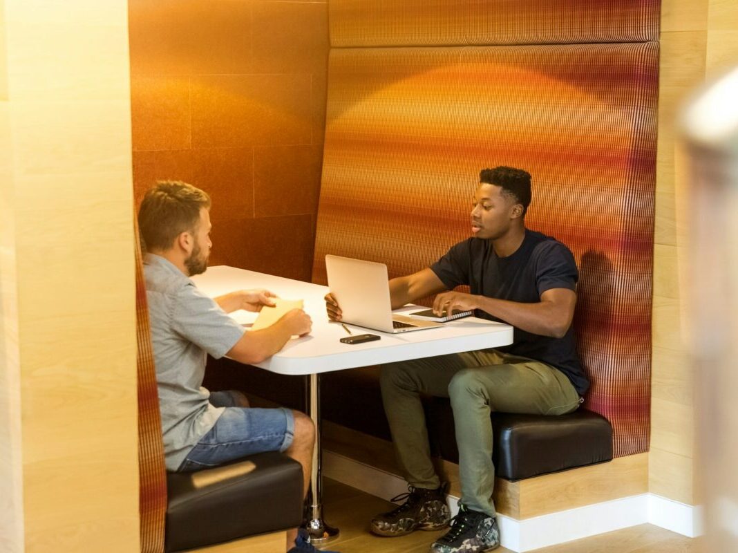 two men sitting across from each other in a booth having a business meeting