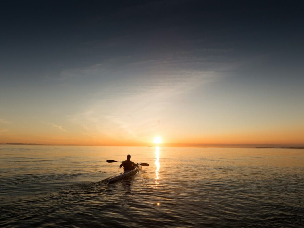 guy in a kayak on water at sunset