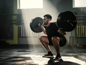 Man squatting with barbell at CrossFit gym.