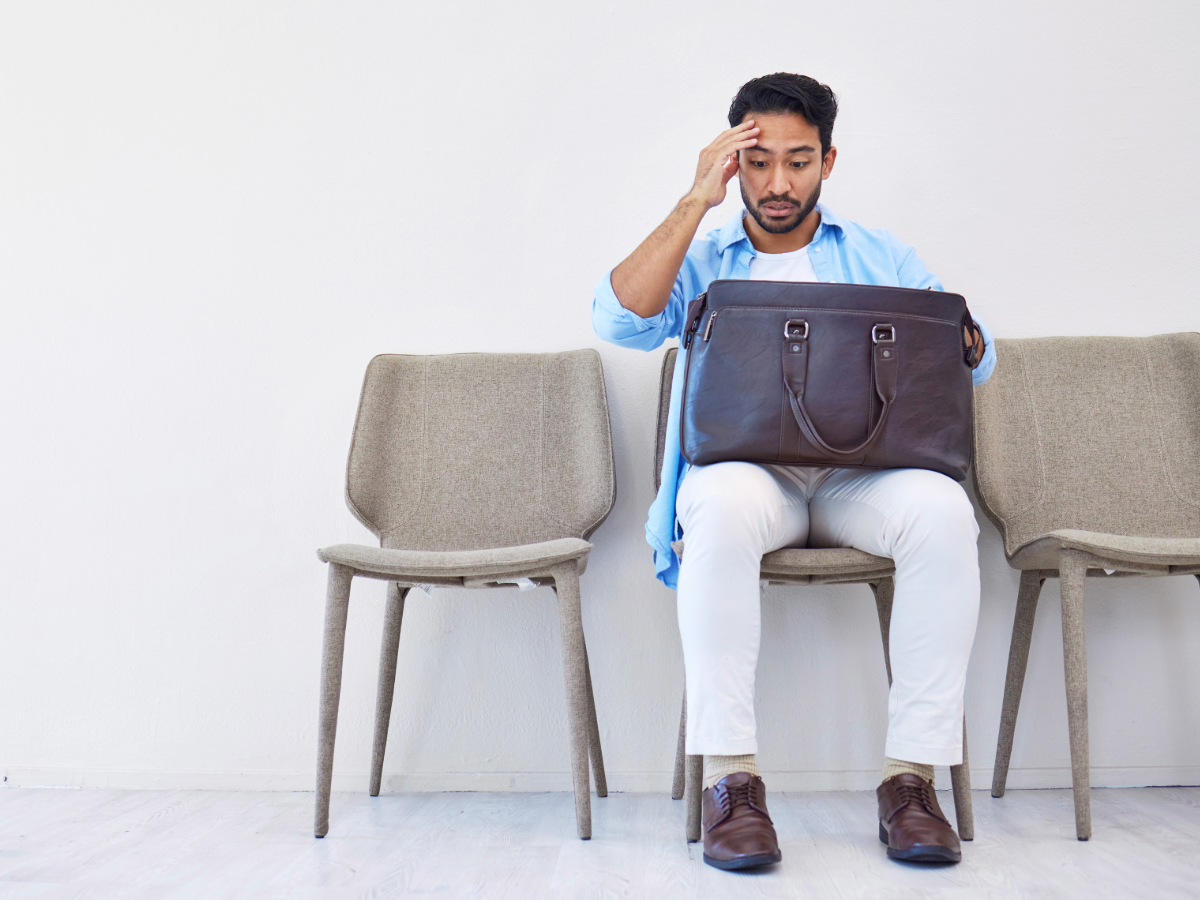 Man sitting waiting for job interview and has his briefcase on his lap and his hand on head like he forgot to bring something.