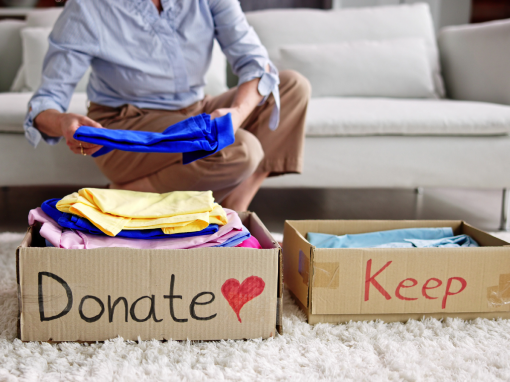 Woman sitting on couch with donate and keep boxes in front of her as she sorts clothes.