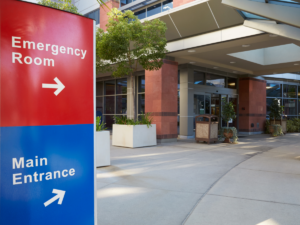 Sign that says "Emergency Room" and "Main Entrance" with arrows pointing to hospital entrance.