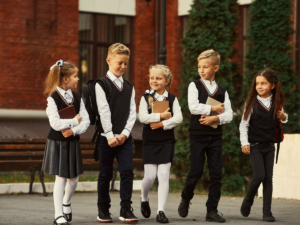 5 children walking out of school wearing school uniforms.