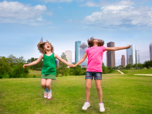 2 Girls jumping in park in front of Houston, TX skyline.