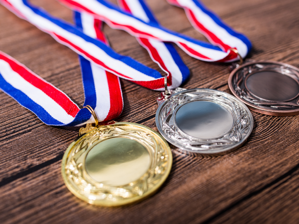 1st, 2nd, 3rd place medals stacked on table with red, white and blue ribbons attached.